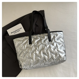 Detail view of silver quilted tote bag with diagonal stitching and black leather handles