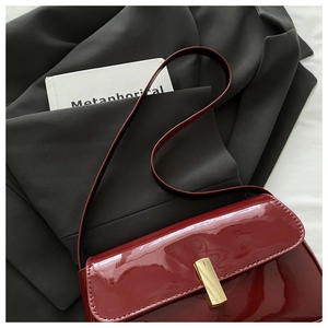 Detail of red patent leather shoulder bag with a bold gold rectangular buckle on suit