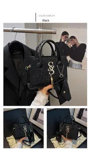 Detail of black crocodile texture handbag with gold S metal logo and tassel charm