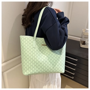 Close-up of mint green tote bag featuring M-pattern print and golden metallic logo plate