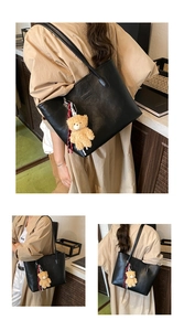 Detail of black leather tote bag with plush bear charm and embossed fashion text logo