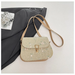 Detailed close-up of floral embroidery on straw bag with gold buckle and leather trim
