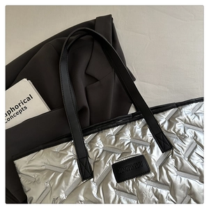 Detail of silver quilted tote bag showing metallic texture and black logo patch