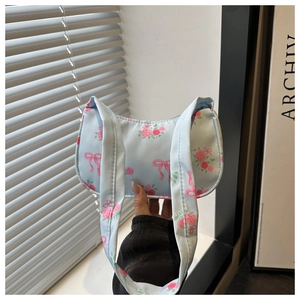 Close-up of light blue shoulder bag with pink floral rose and bow prints on soft canvas