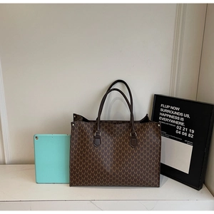 Close-up of large brown tote bag with M-letter monogram and leather handles