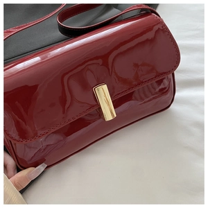 Detail of red patent leather shoulder bag with a sleek gold metal buckle closure