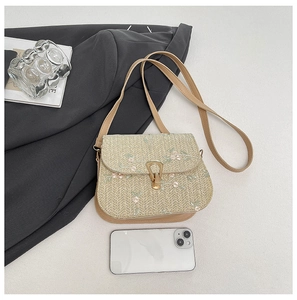 Detailed embroidery of white flowers on a natural straw crossbody bag with gold lock