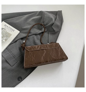 Detail of dark brown pleated rectangle shoulder bag placed on a grey blazer suit