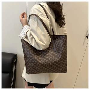 Detailed view of large brown tote bag with M-pattern print worn by a model