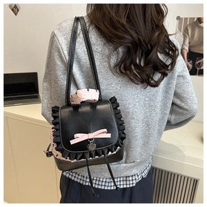 Détail d'un mini sac à dos noir en similicuir avec nœud rose et pendentif en cœur