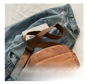 Close-up of brown corduroy crossbody bag with adjustable strap on denim background