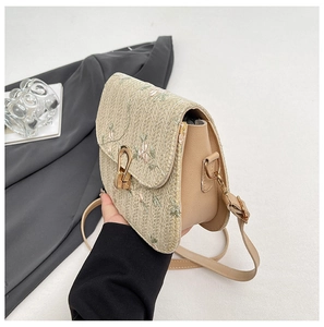 Detail of straw woven crossbody bag with floral embroidery and gold metal clasp