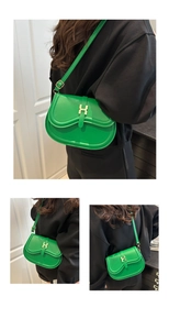 Detail of green leather saddle bag with gold H clasp and adjustable shoulder strap