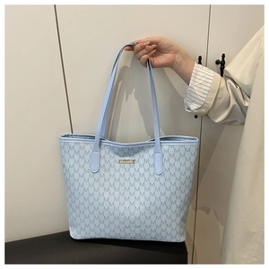 Detail of light blue tote bag with repeating M-letter prints and gold metal plate