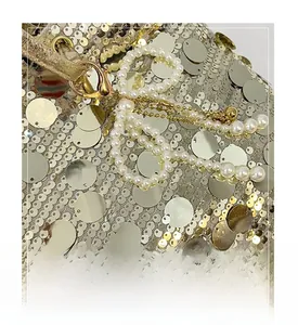 Close-up of pearl bow charm with gold lobster clasp on sequined shoulder bag surface