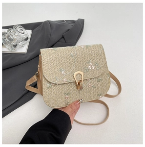 Detail of floral embroidery and golden horseshoe clasp on beige straw woven bag