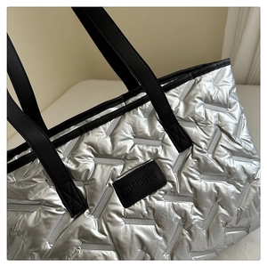 Detail of silver quilted tote bag with geometric stitching and black brand label tag