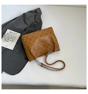Detail of brown leather tote with embossed logo patterns and metal chain strap