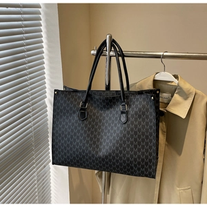 Close-up of black tote bag with gray M-letter print and reinforced metal rivet details