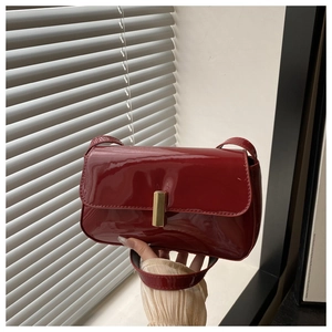 Detail of red patent leather shoulder bag with a rectangular gold metal buckle closure