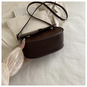 Detail of dark brown leather crossbody bag with minimalist gold metal buckle and texture