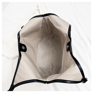 Internal view of a black tote bag showing beige herringbone lining and a magnetic silver clasp