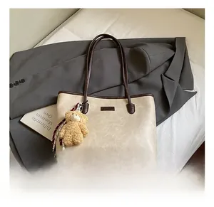Detail of off-white tote bag with brown straps and a cute bear charm on a suit background