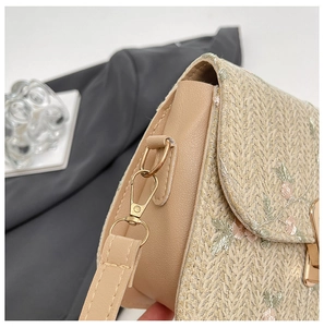 Close-up of floral embroidery on straw crossbody bag with golden metal buckle clasp