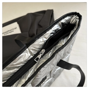 Detail of silver quilted tote bag featuring black zipper and metallic puffer texture