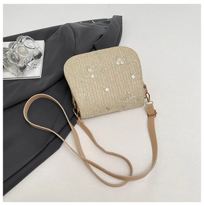 Detailed embroidery on a beige straw crossbody bag with floral patterns and leather strap