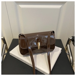 Detail of glossy brown patent leather shoulder bag with a rectangular gold buckle closure