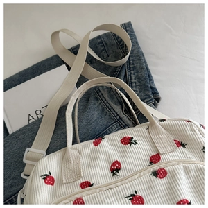 Gros plan de broderies fraises sur un cabas en velours côtelé écru avec sangle