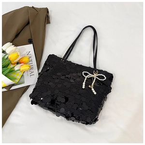 Detail of black sequined tote bag featuring a decorative white pearl bow charm
