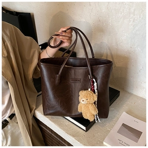 Detail of dark brown leather tote bag with FASHION lettering and plush bear charm