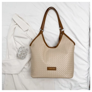 Detail of minimalist beige woven tote bag with brown leather trim and metallic rings