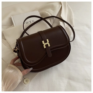 Detail of dark brown leather saddle bag featuring a gold H-shaped clasp and adjustable strap