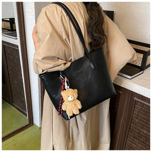 Detail of black faux leather tote bag with FASHION embossment and plush bear charm