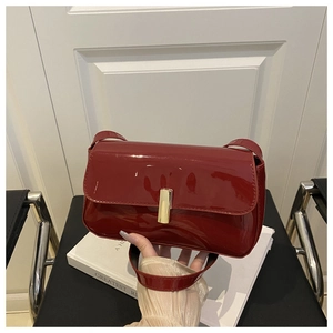 Detail of a dark red patent leather shoulder bag with a gold rectangular buckle