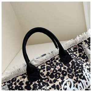 Macro view of leopard print tote bag with white tassel fringe and cursive print