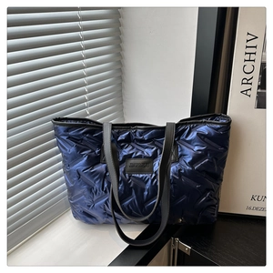 Detail of blue quilted nylon tote bag with black logo patch and soft padded texture
