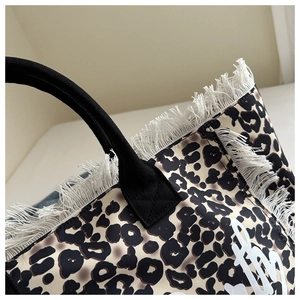 Detail of leopard print tote bag with white tassel edges and black woven handles