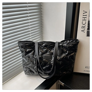 Close-up of black puffer tote bag showing geometric quilted texture and logo tag