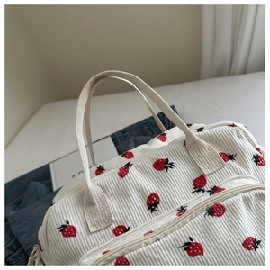 Gros plan de la broderie fraise sur le sac à déjeuner en velours côtelé blanc et anse