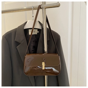 Detail of dark brown patent leather shoulder bag with golden metallic clasp and strap