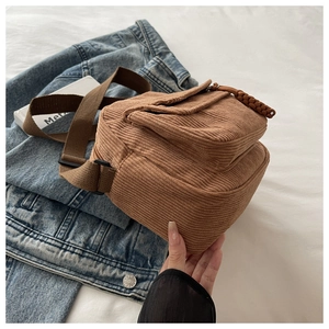 Close-up of brown corduroy crossbody bag featuring a front pocket and woven zipper pull