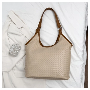 Detail of beige woven tote bag with dark brown leather strap and silver metal buckle