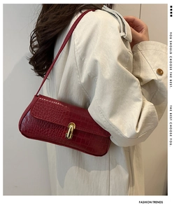 Detail of dark red crocodile embossed baguette bag with gold buckle on trench coat