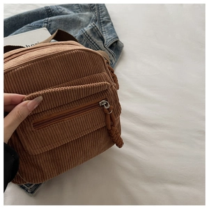 Detailed close-up of brown corduroy crossbody bag texture and front zipper pocket