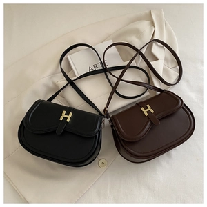 Detail view of leather saddle bags with gold H-shaped buckle on a textured background