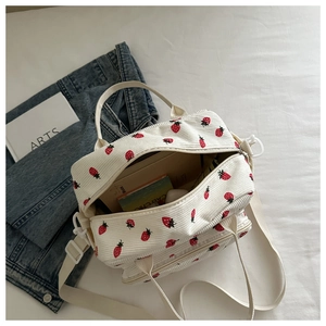 Détail du sac en velours côtelé à fraises montrant les doubles zips et la bandoulière blanche